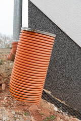 A thick drainage pipe protruding from the ground near a house, part of the water management system,...