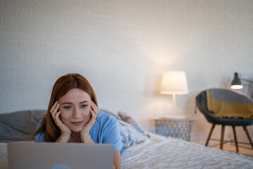 Woman lying on bed using laptop in cozy bedroom