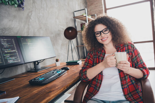 Young woman programmer with curly hair working remotely in a modern home office with cozy atmosphere and stylish casual attire