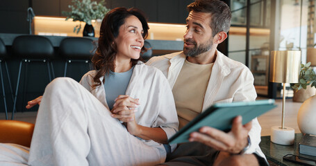 Obraz premium Mature couple, tablet and talk on sofa, smile and memory with streaming, video or film on web in home. People, man and woman with digital touchscreen, app and choice for movies in lounge at apartment