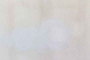 White textured wall with visible pale paint patch. Rough stucco or plaster surface showing slight...