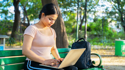 Young beautiful Indian woman working on a laptop sitting in the park, college student or business women remote work concept