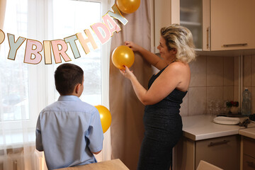 A woman with her son and nephew decorate a room and a festive table for a birthday celebration. Soft lighting.