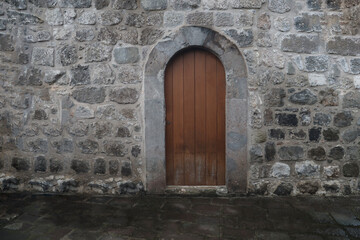 Ancient arched wooden door in stone wall. old wood door frame in stoned fence building. Medieval Arch Wooden Closed Castle Gate. Historical background.