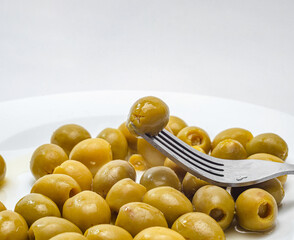 Green olive on fork above a plate of olives for a savory mediterranean snack
