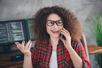 Young female programmer working remotely, wearing casual checkered shirt, coding on computer,...
