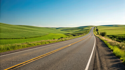 Fototapeta premium A smooth two-lane highway winding through rolling green fields under a clear blue sky, creating a tranquil, scenic drive with a limitless sense of exploration.