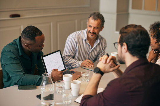 High angle view of businessman showing data on laptop to coworkers during meeting in creative office