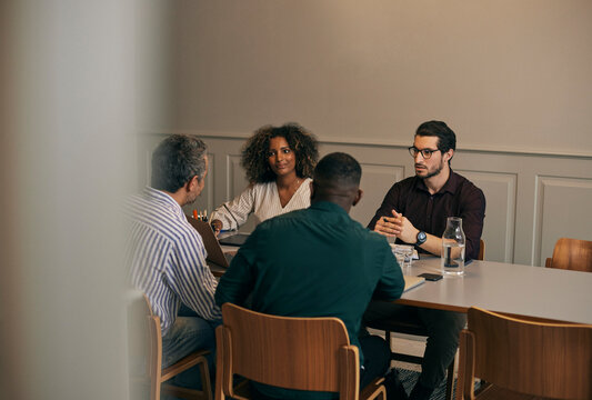 High angle view of male and female creative business professionals discussing with each other while sitting in meeting r