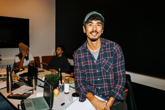 Portrait of smiling male student wearing cap sitting on table in classroom at college