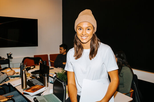 Portrait of happy female student wearing knit hat sitting on table in classroom at college