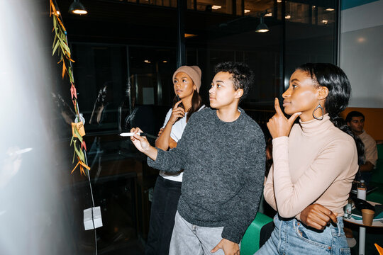 Young man holding felt tip pen while standing with female friends and planning at college
