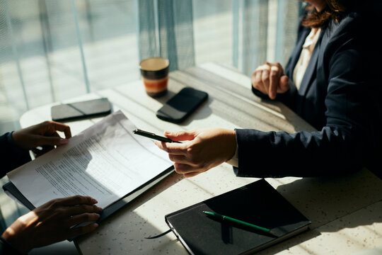 High angle view of female client giving pen to businesswoman holding contract at table in office