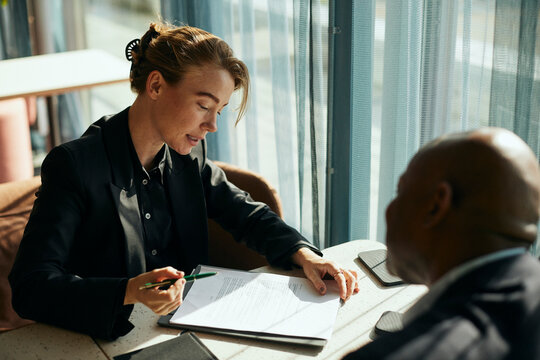High angle view of businesswoman explaining instructions of business contract to male customer while sitting at table in
