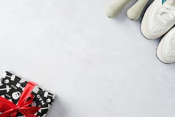 Fitness-themed gift box with red ribbon, white sneakers, and dumbbells on a marble surface. Perfect...