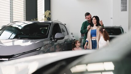 Husband blindsides wife at car dealership giving her a gift of a new car next to the kids. The concept of buying a new car.