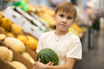 Fototapeta premium Kid teenager shopping for fresh organic fruits and vegetables in supermarket. Cute boy holding watermelon in a hands.
