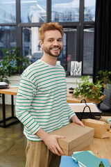 Fototapeta premium Smiling man enjoys the process of packing and moving in a modern workspace filled with plants