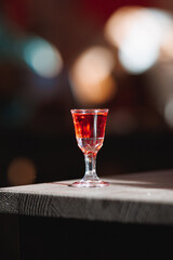 A shot glass of red liquid sits on a wooden table