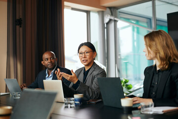 Mature businesswoman discussing with male and female colleagues during meeting in board room at office