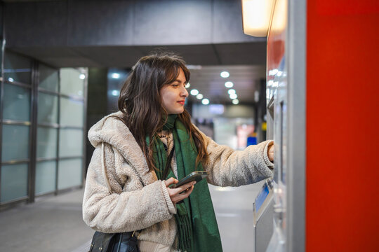 Young woman buying metro ticket from a machine

