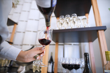 A person is skillfully pouring a rich, red wine from a bottle into a gleaming glass, creating a delightful experience