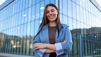 Fototapeta premium Smiling businesswoman with crossed arms posing in front of modern office building