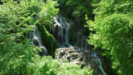 Water cascades over mossy limestone terraces, framed by vibrant green foliage in a lush forest setting at Krushuna waterfalls. - Powered by Adobe