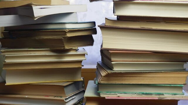 Person removes stacked literature study books from desktop workspace CLOSE-UP