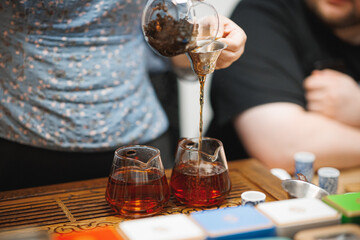 A person is skillfully pouring tea into two glasses that are placed on a table, creating a cozy atmosphere for refreshments