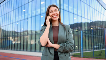 Smiling businesswoman making a phone call outside modern office building