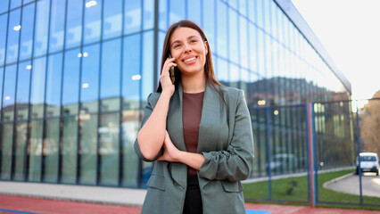 Smiling businesswoman making a phone call outside modern office building