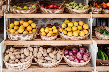 Baskets of fruit and vegetables in a market: potatoes, pears, apples, onions, citrus fruits, peppers, garlic. Front view.