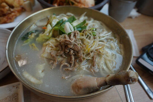 Korean dak hanmari kalguksu served with whole chicken leg and rich broth in a brass bowl