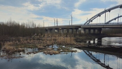Highway bridge over a reflective river surrounded by nature on a cloudy day
