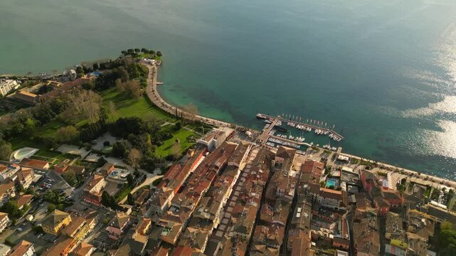 drone above epic video of harbour with boats in Italian Bardolino at Lake Garda with red piled roofs and clear transparent blue water 