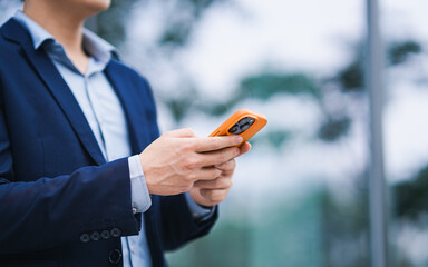 Man texting on phone in city: A sophisticated man, elegantly dressed in a business suit, engrossed in his phone, his focus mirroring the technological rhythm of the city. 