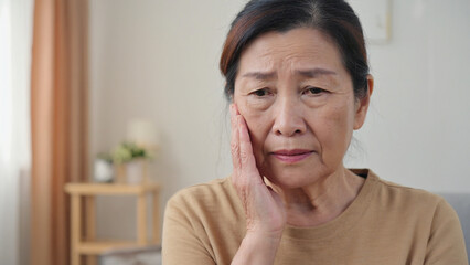 Distress and Discomfort: A close-up portrait of an elderly woman in her home, showing evident signs of pain and discomfort, as she touches her face.