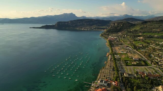 aerial drone scenic video of sailing boats in raws in harbour, coastal village with red roofs at Italian Garda lake in sunny day