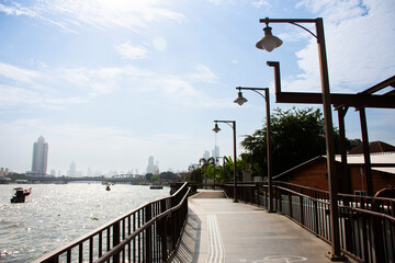 Fototapeta premium View landscape chao phraya river and cityscape with footpath walkway bridge on riverside for thai traveler people walking travel visit Kudeejeen village of Kudi Chin town historic in Bangkok, Thailand