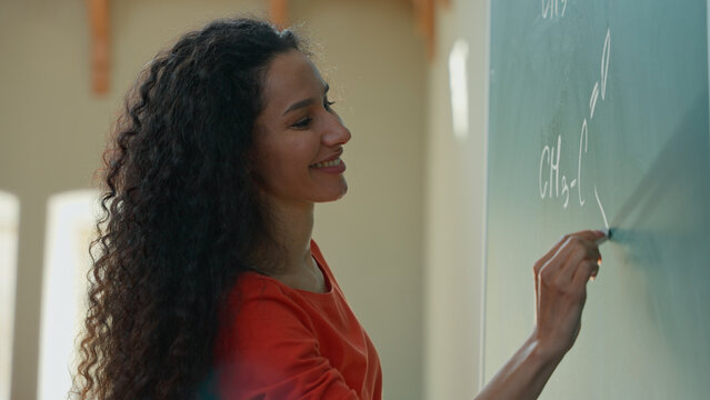 Smiling clever Hispanic student girl Latina woman Caucasian female lady teacher tutor studying learn writing chalk on blackboard formula math mathematic in class auditorium university college academy