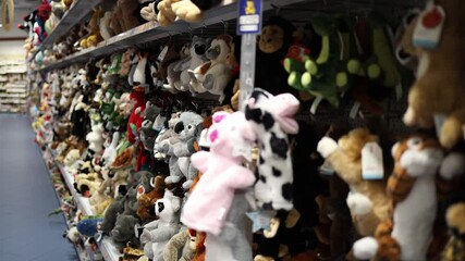 Aisle filled with colorful plush toys in a toy store. Rows of stuffed animals including koalas, cows, lemurs, and dinosaurs create a cheerful and playful atmosphere for children and families.