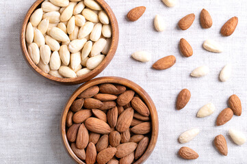 Almonds, with seed coats and blanched, in wooden bowls, on linen fabric. Fruits of Prunus amygdalus, syn. Prunus dulcis, ready-to-eat as snack or as ingredient for baking. Close up from above. Photo