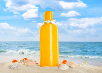 Bottle of sunscreen product and shells on sandy beach near sea