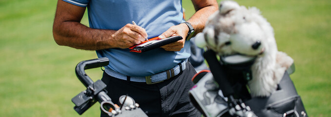Midsection of golfer writing on score card standing at golf course