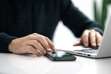Closeup image of a male hands using smartphone and laptop. Boy working online, internet applications