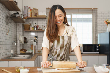 Young woman rolling dough on kitchen counter while man prepares in background of cozy modern kitchen
