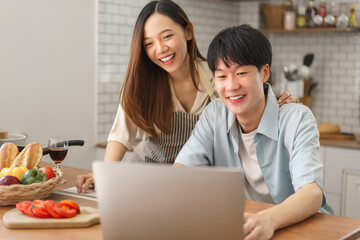 Joyful couple enjoying video call together in kitchen with fresh food and drinks on the counter..