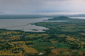 Scenic Landscape from Above: An aerial view showcases a breathtaking landscape with a vast lake mirroring the overcast sky, interspersed with green farmlands and distant hills.