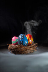 Nest filled with colorful decorated easter eggs on a dark background. Smoke or fog effect. Concept of celebrating the easter holiday